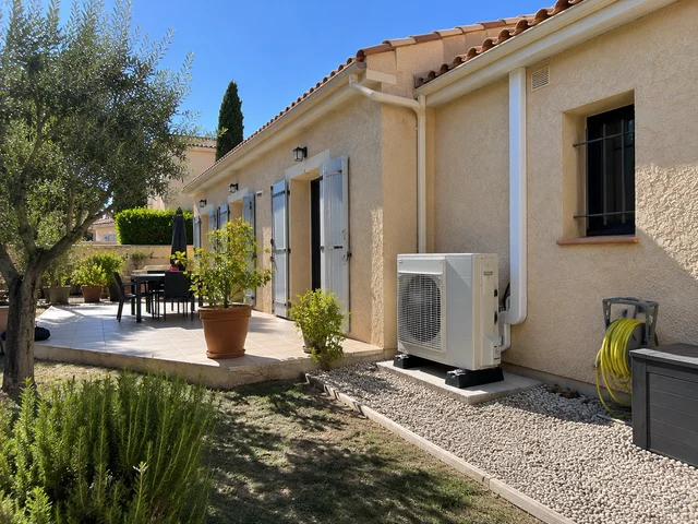 Groupe extérieur de pompe à chaleur au pied d’une maison avec terrasse et olivier